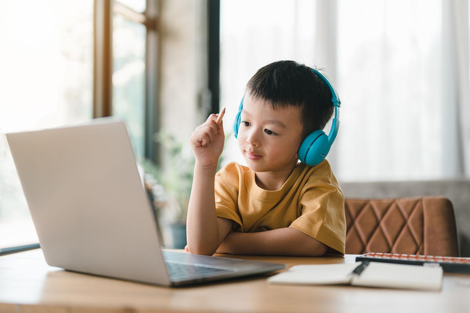 Kindergarten child writing at a desk with headphones and worksheets