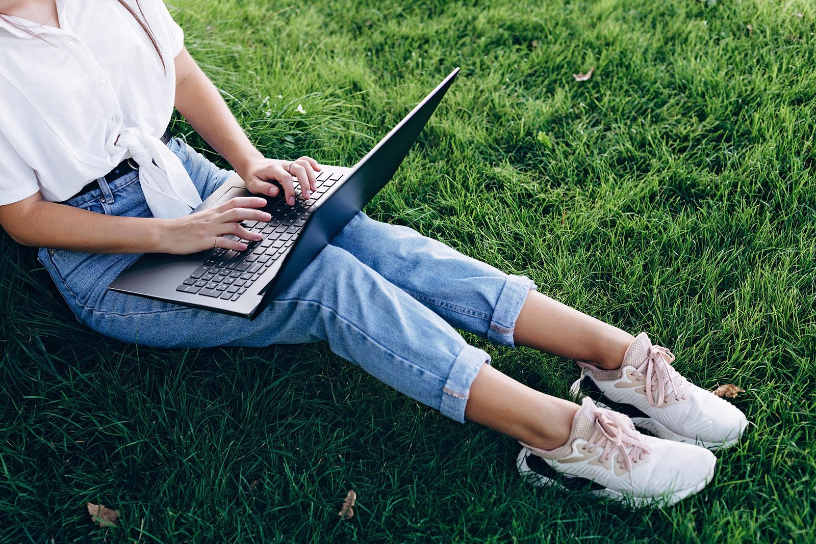 Teenage girl sitting on grass completing school outside on computer