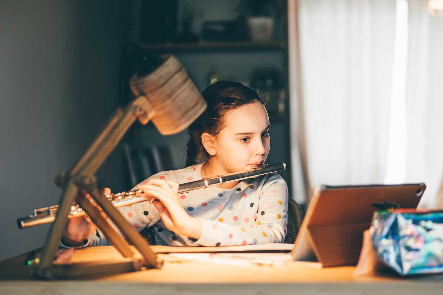 Talented young online school student playing the flute in bedroom