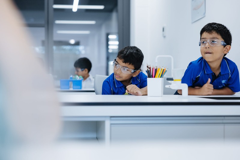 Junior school students in science classroom wearing safety glasses with coloured pencils on desk