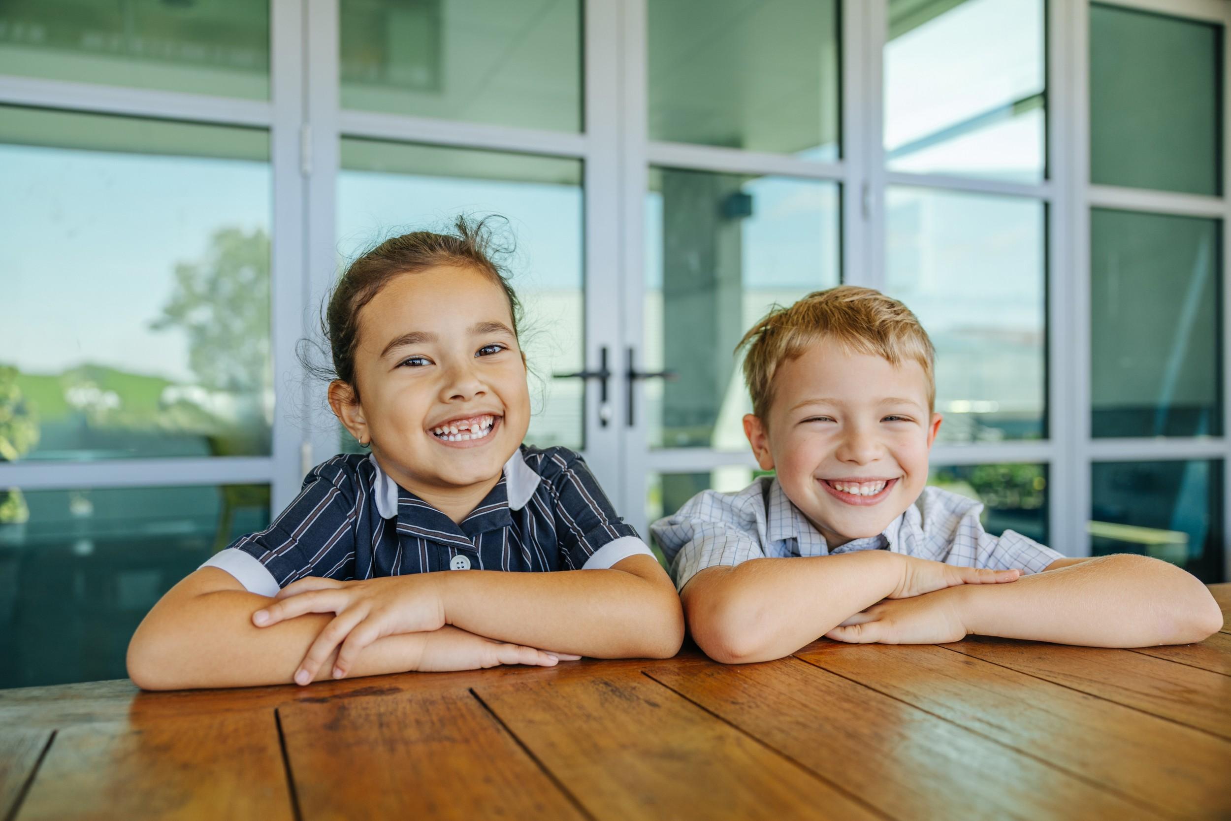Two primary students smiling together at a table on campus at ACC Moreton.