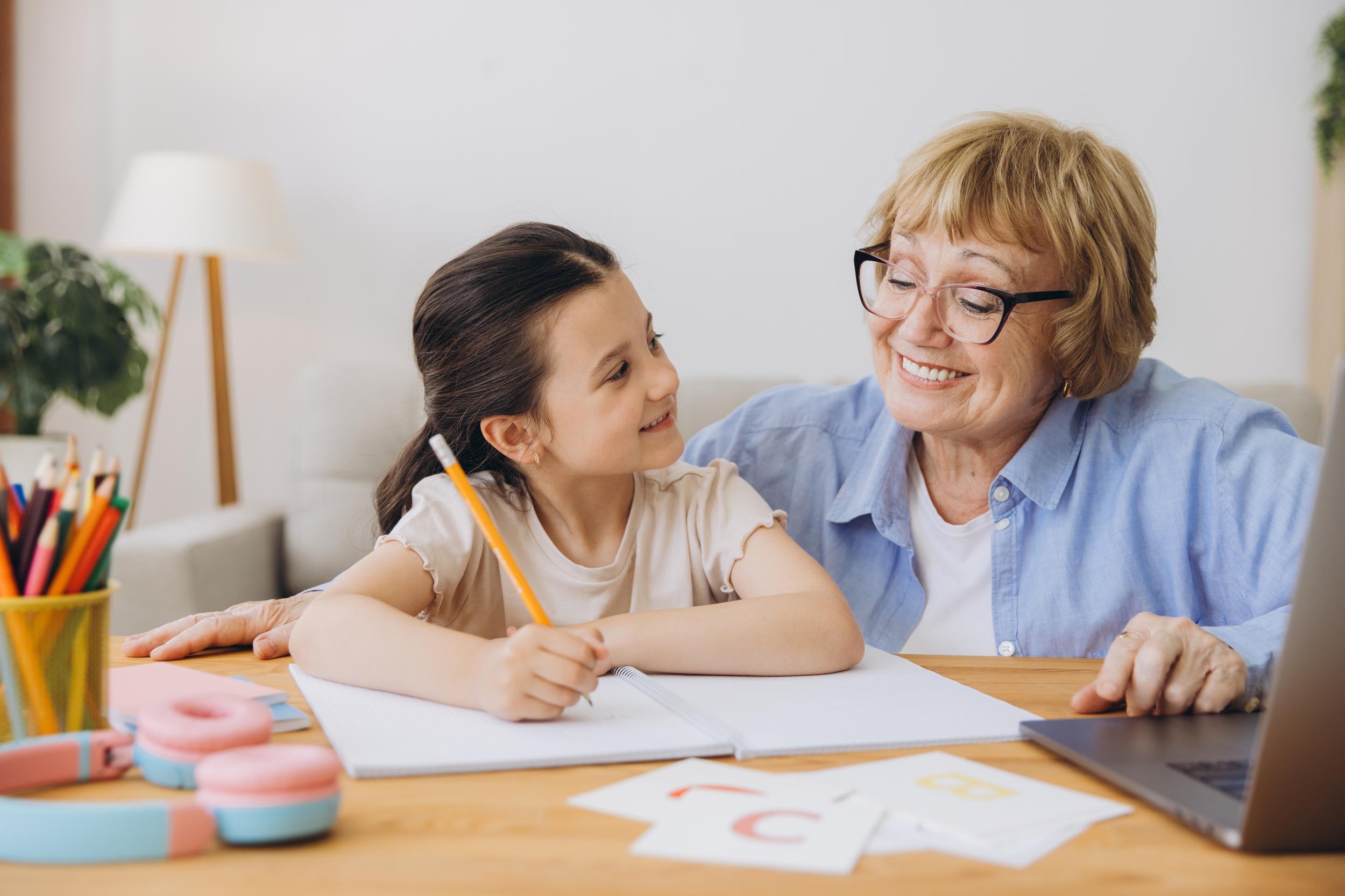 A child and an older woman smile at each other while sitting at a table with stationery