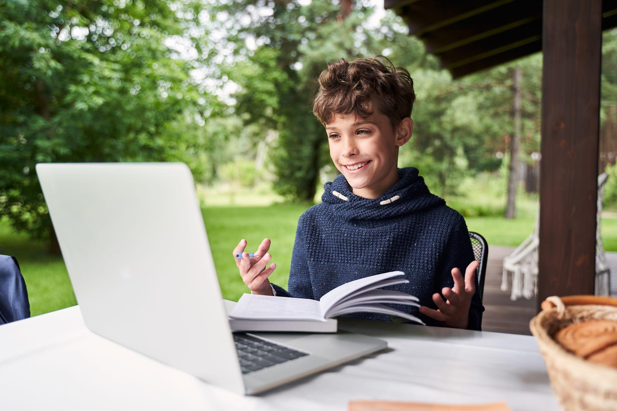 A student at ACC Moreton engages in online learning outdoors, smiling while using a laptop and holding