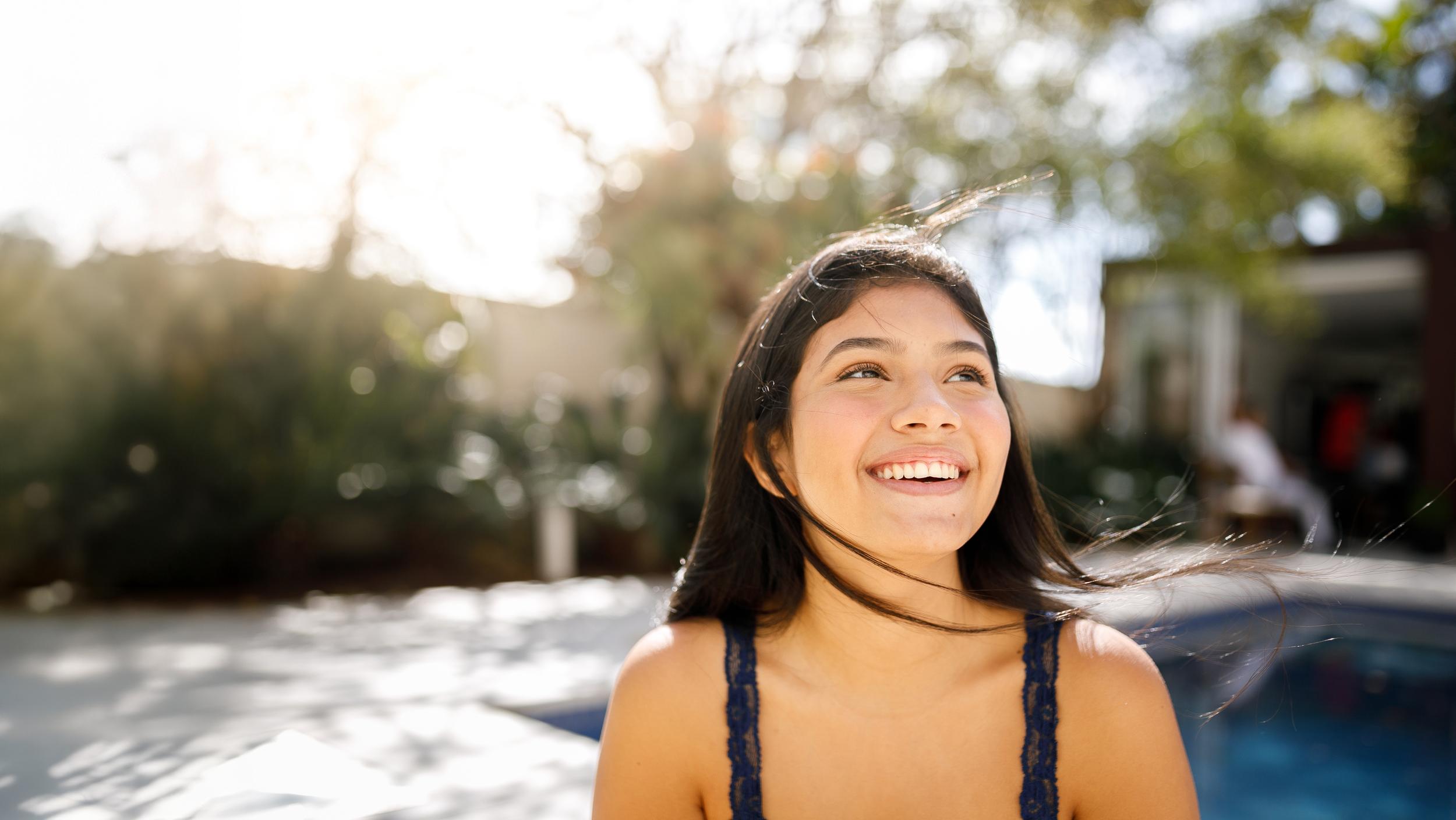 A student smiles while sitting outdoors near a pool, enjoying a sunny day at ACC Moreton.