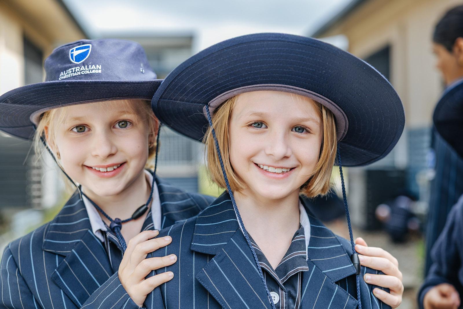 Two ACC Moreton primary students in uniforms and school hats smiling together