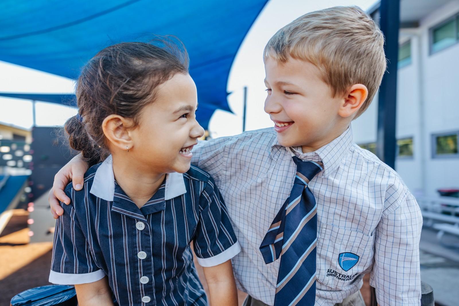 Two ACC Moreton students in uniform smiling together in the playground