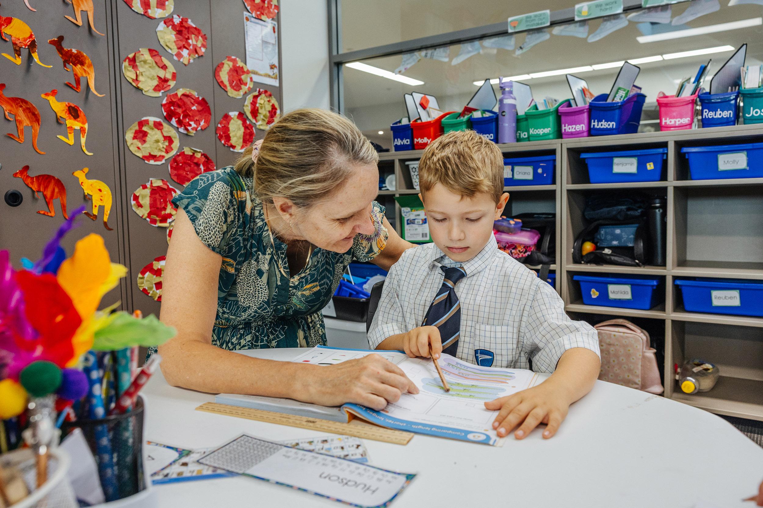 Teacher guiding a primary student through classroom work at ACC Moreton
