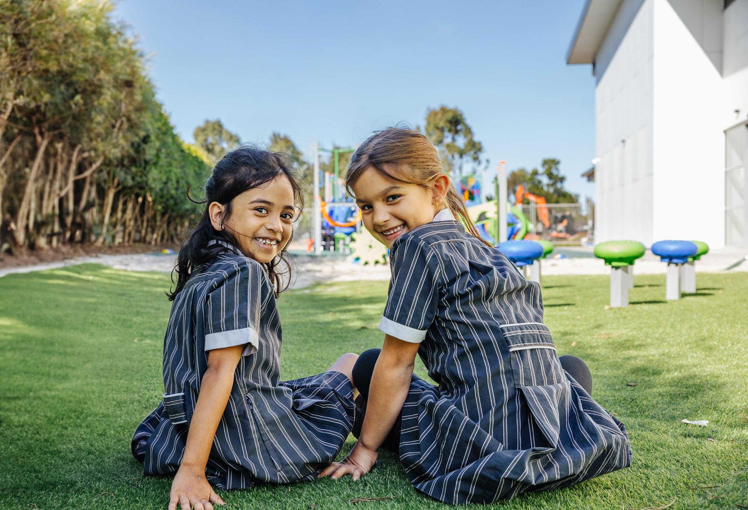 Two primary students smiling on the playground grass at ACC Moreton