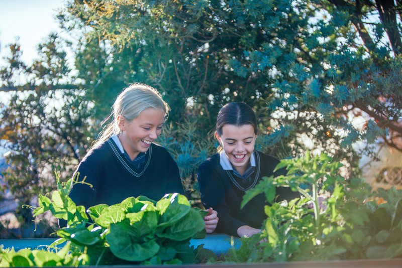 two smiling female students who are friends, working in the garden