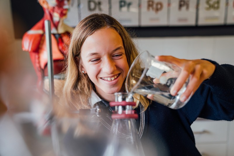 female secondary student in science class pouring liquid from beaker into conical flask