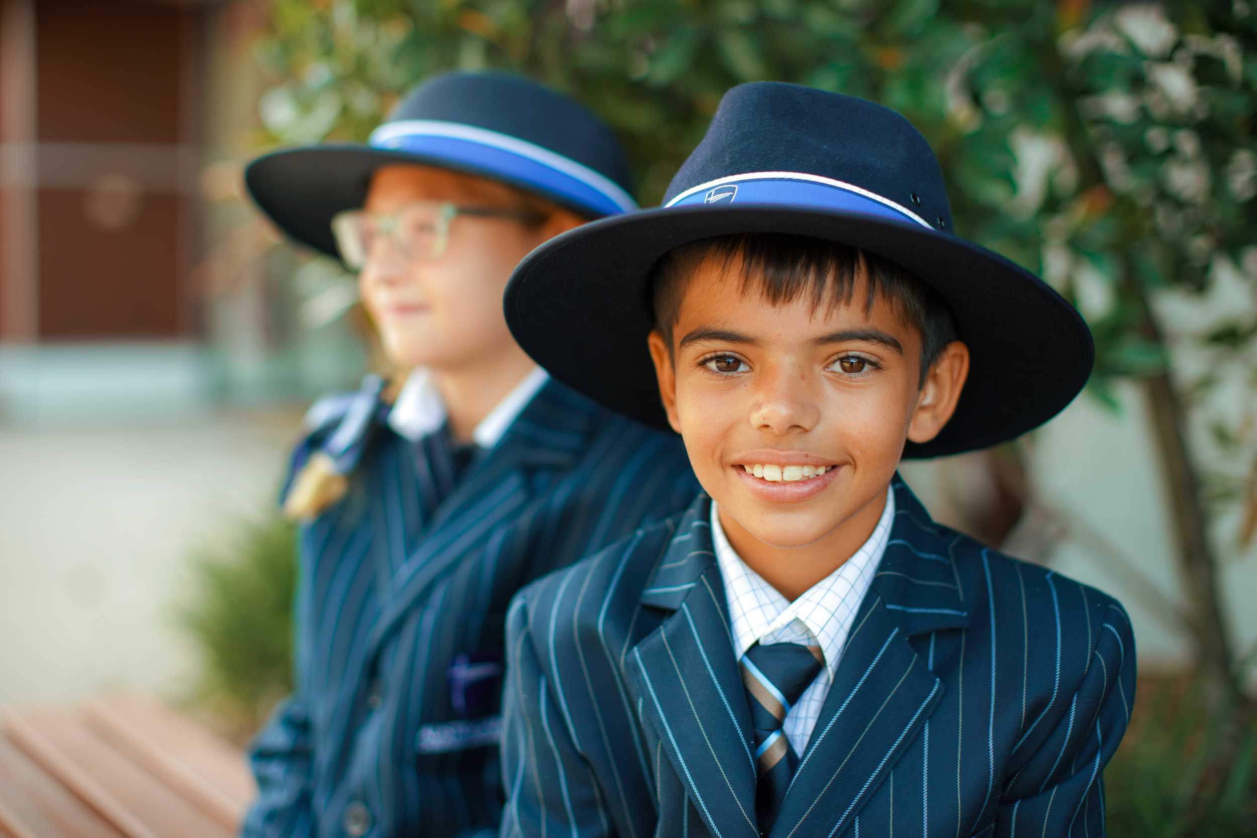 smiling primary school students in uniform wearing blazers and broad brim hats