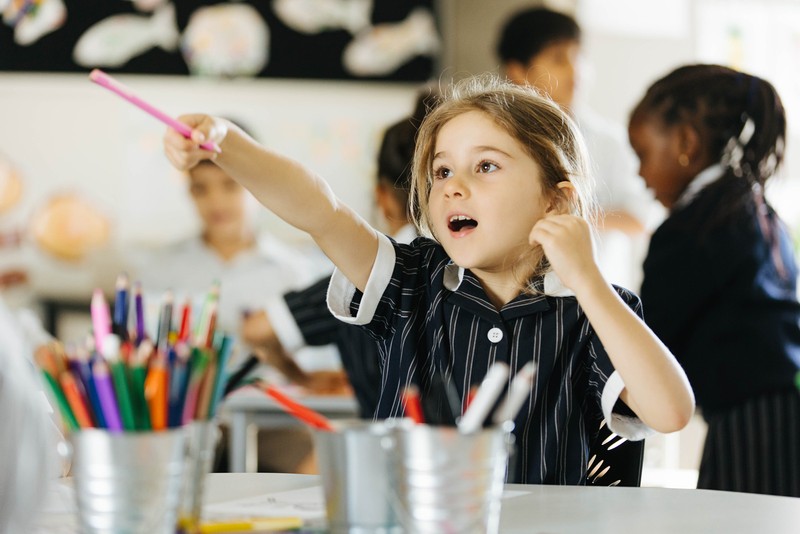 primary school girl sitting at desk with mouth open, point with a pencil