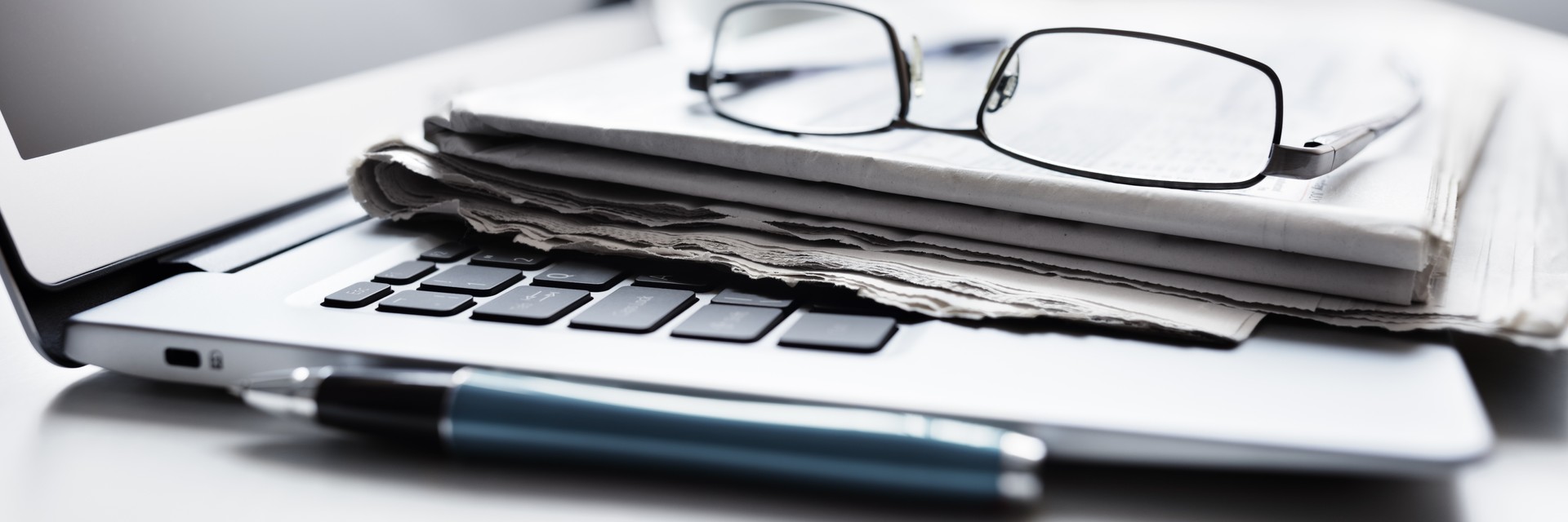 closeup of reading glasses and a notepad sitting atop a laptop with a mug in the background