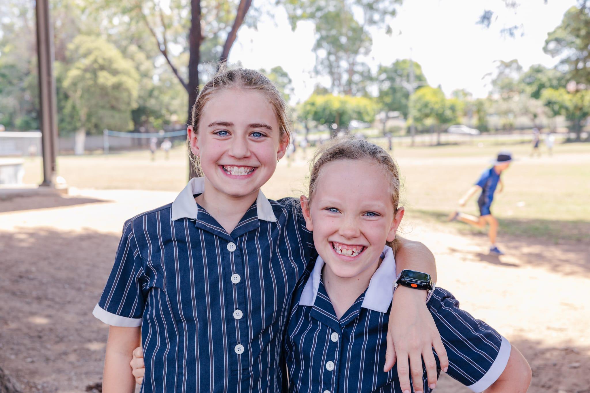 Two smiling students in Australian Christian College Singleton uniforms hugging outdoors, reflecting friendship and Christ-centred values