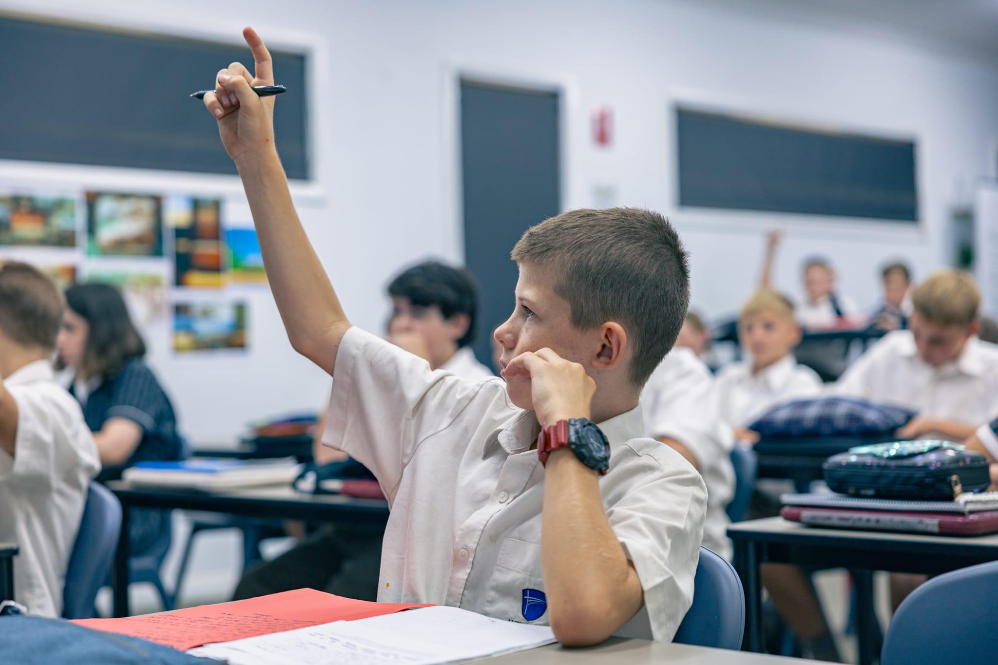 Engaged student raising hand in class at ACC Singleton, reflecting belief-driven academic growth and support