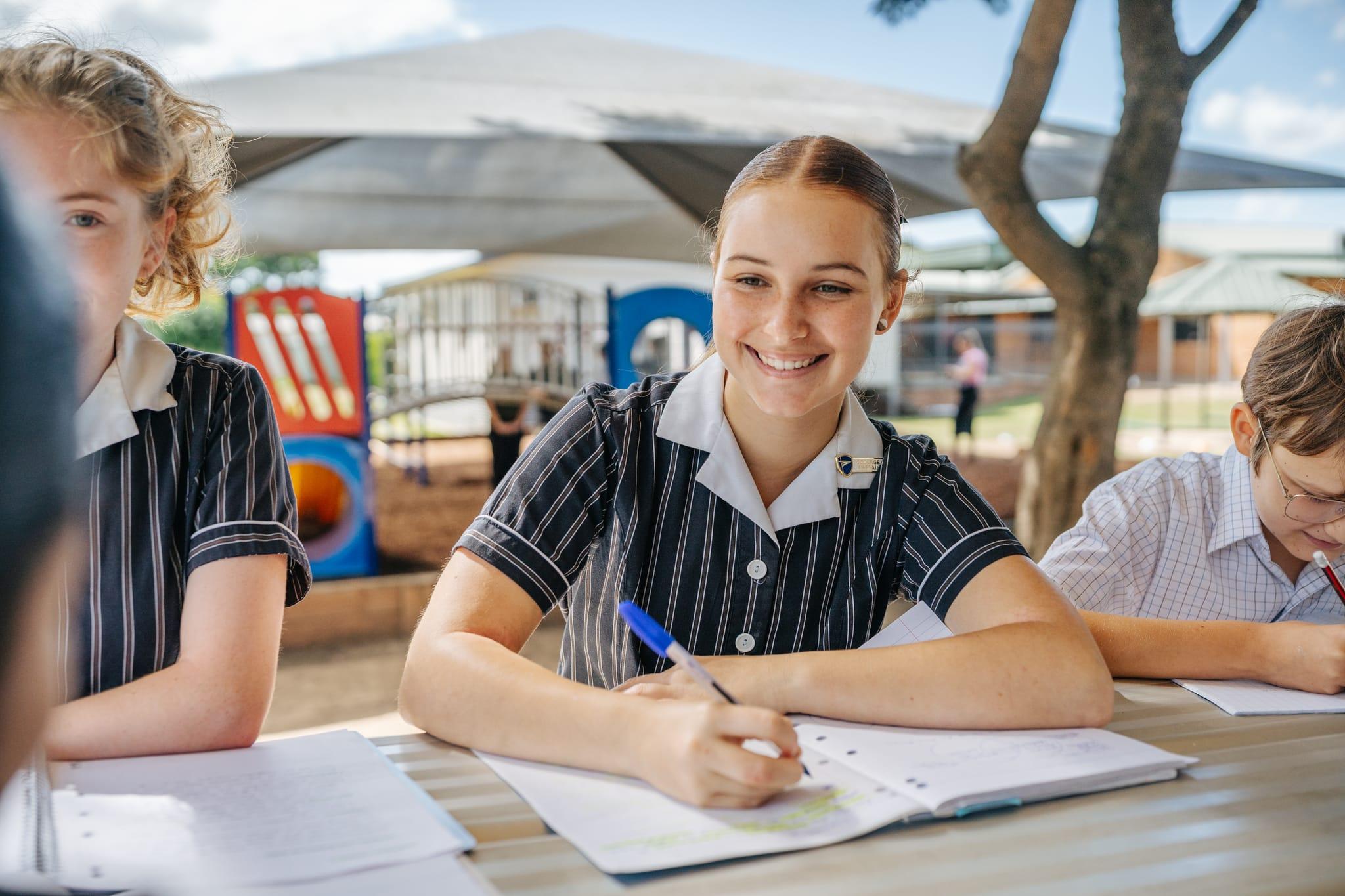 Smiling senior student writing outdoors, representing independent learning and growing confidence in the senior years.
