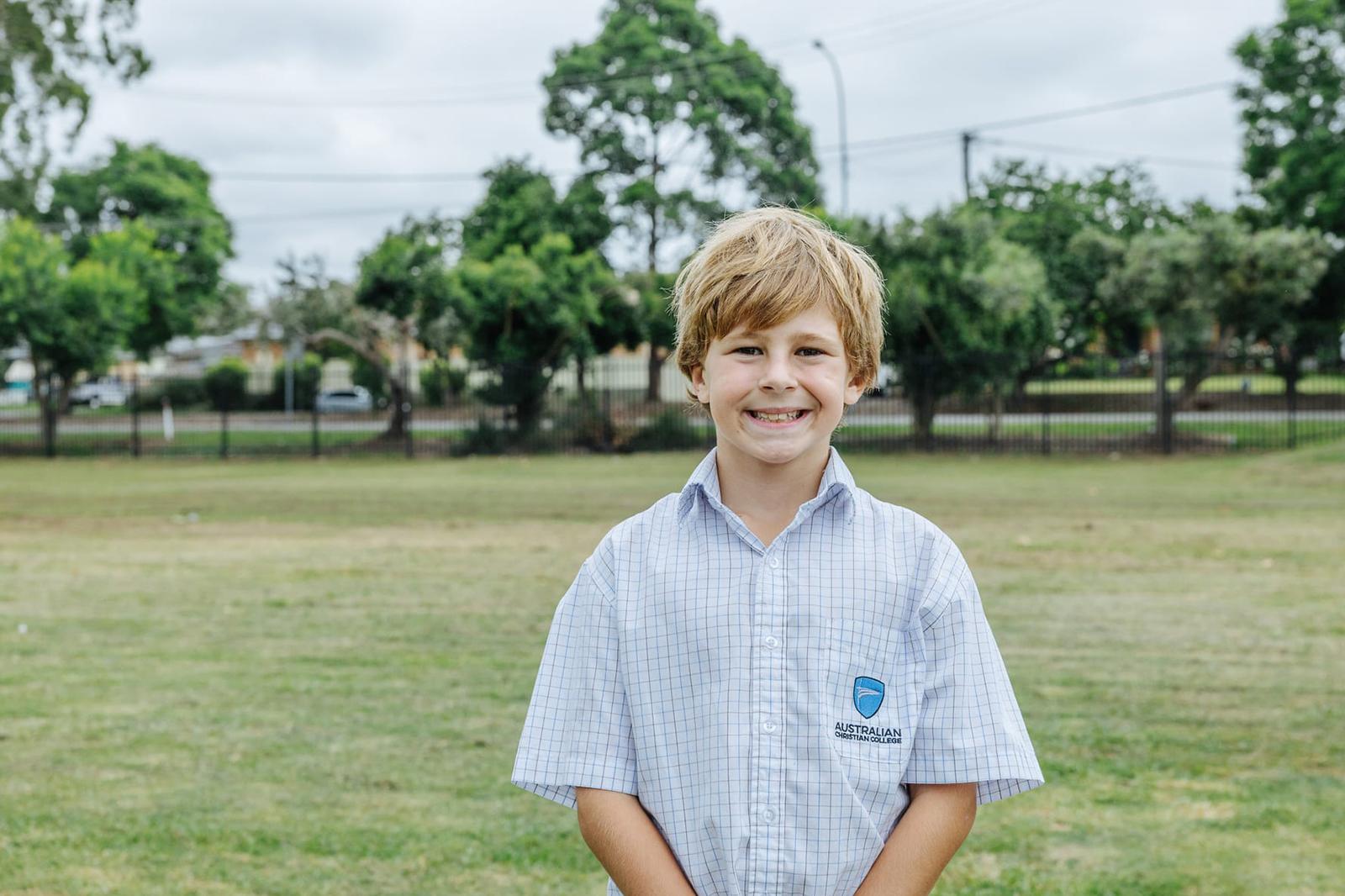 Smiling junior school boy standing on the school oval, reflecting the approachable and inclusive atmosphere of affordable Christian education in the Hunter Region.