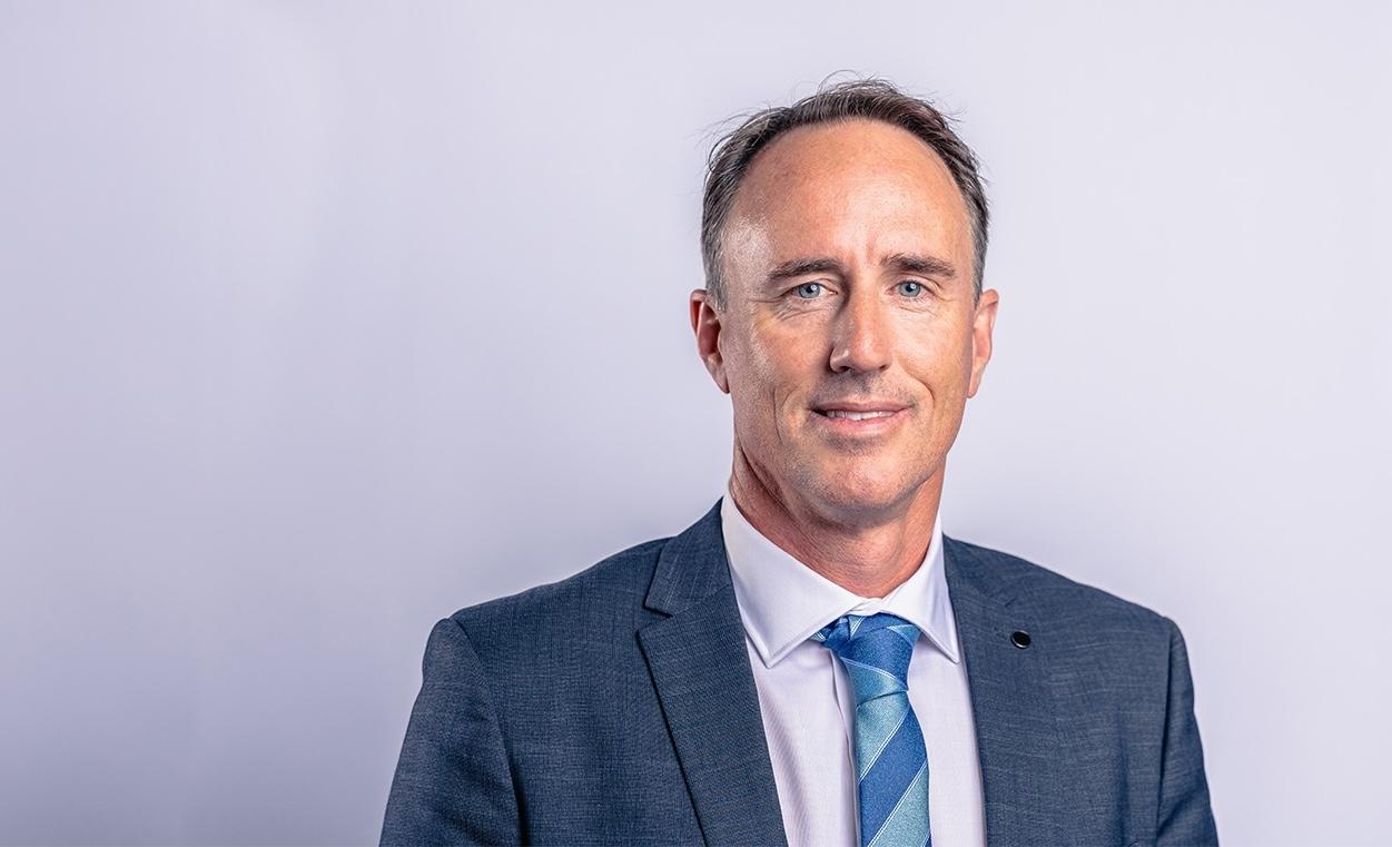 Principal of ACC Singleton smiling, wearing a suit and tie, against a plain background.