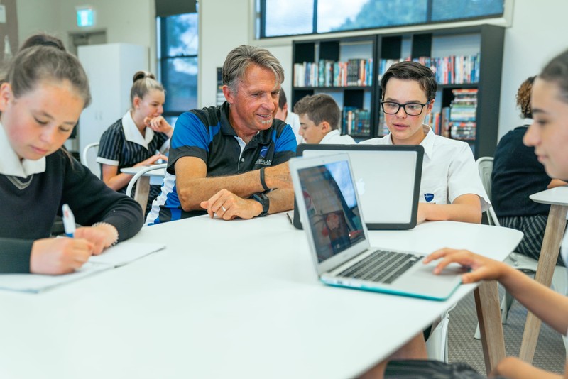 Teacher sitting at desk instructing student with laptop