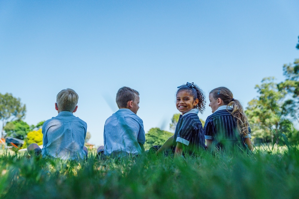 Simling primary school student sitting on grass with supportive friends