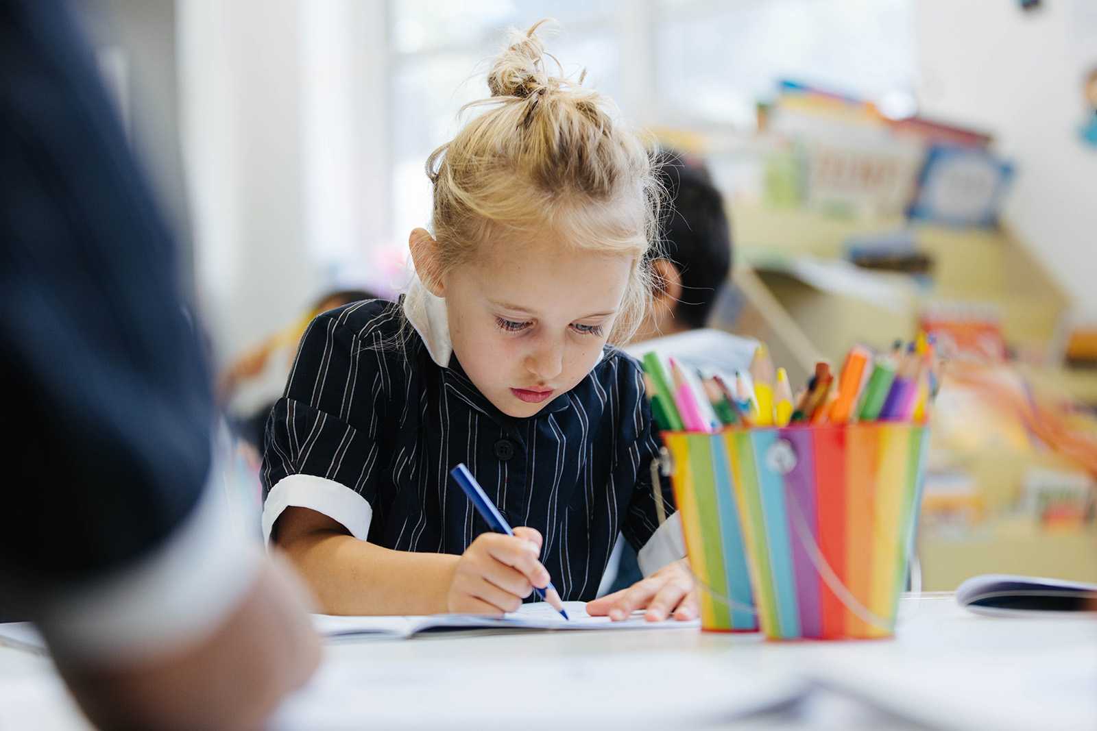 Focused primary school student in formal uniform, drawing with coloured pencils