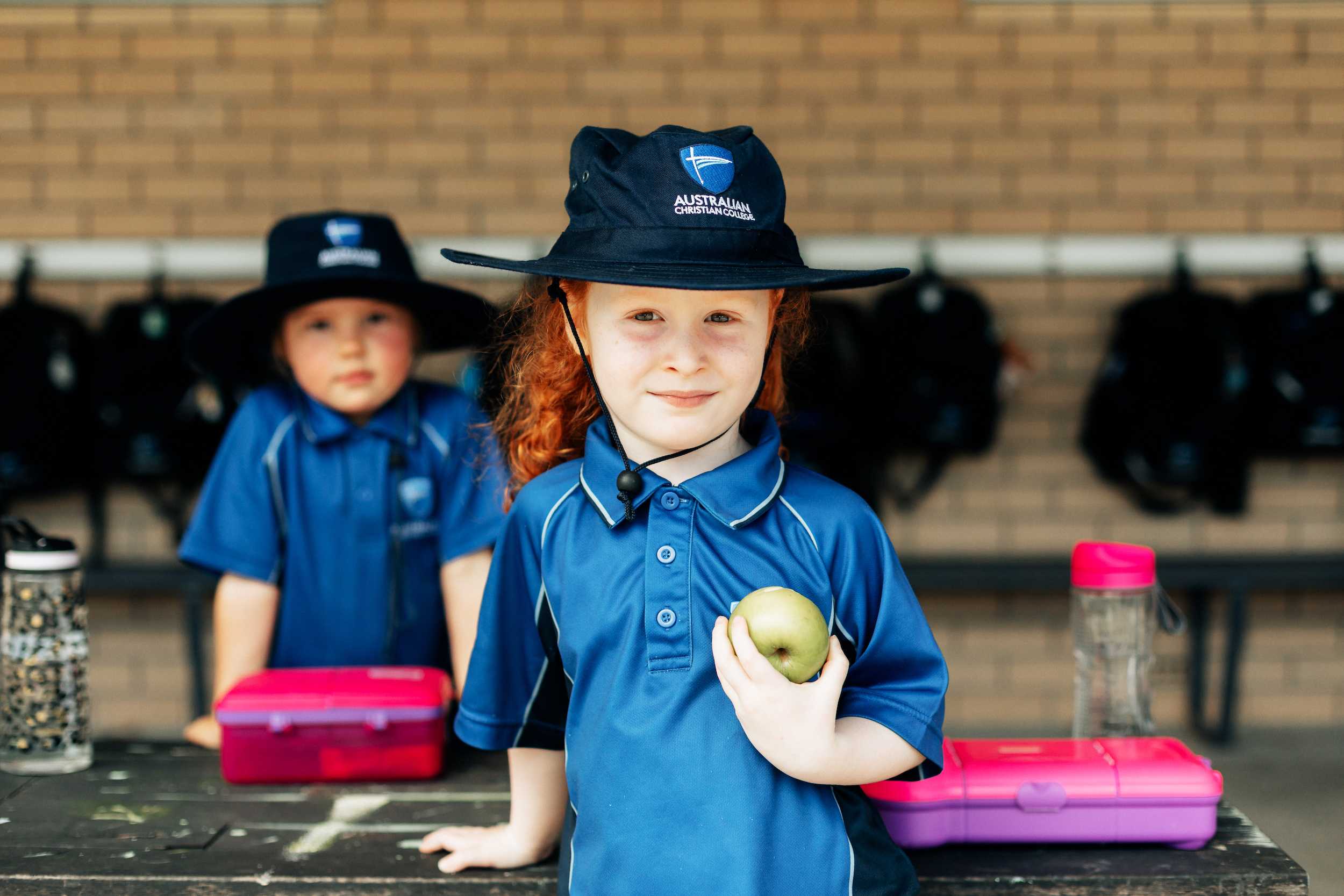 Prep school girl wearing a broad-brim hat and holding an apple at recess