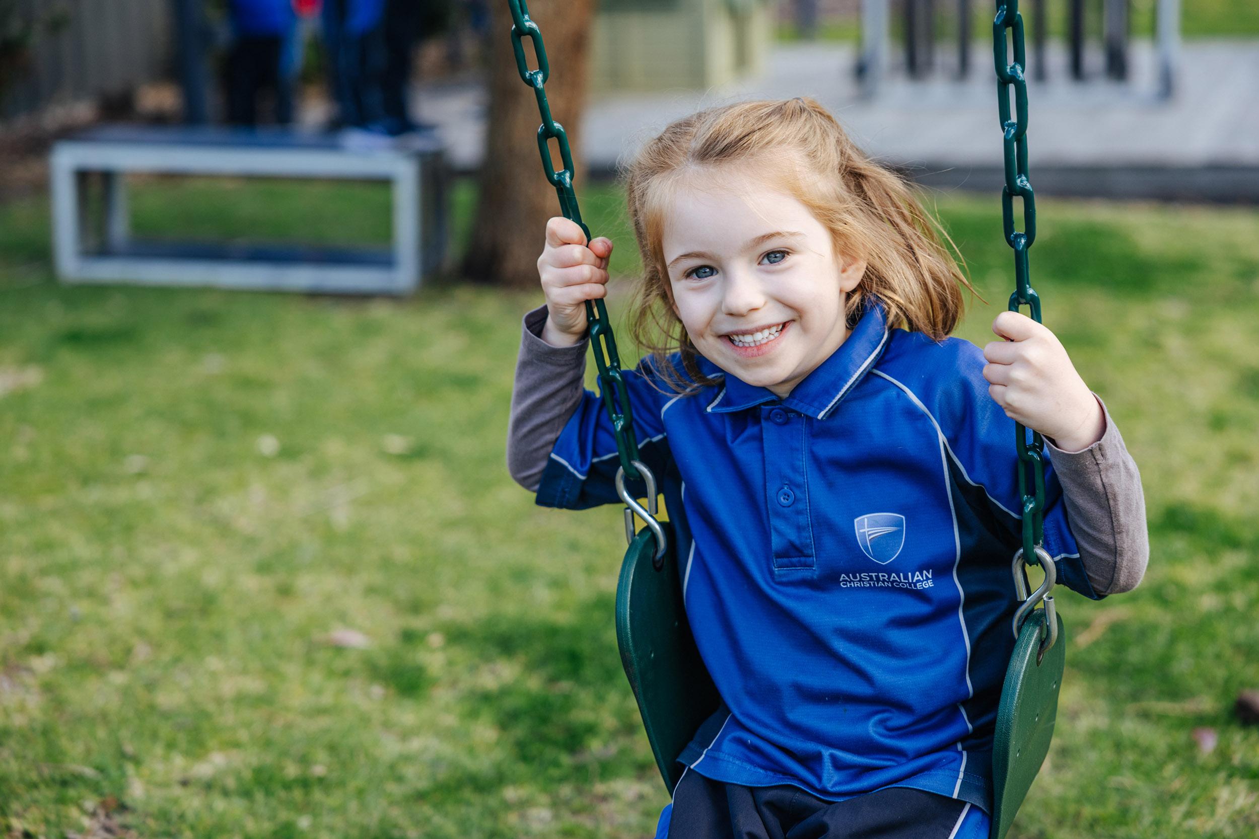 Smiling kindergarten girl on a playground swing in ACC Southlands uniform
