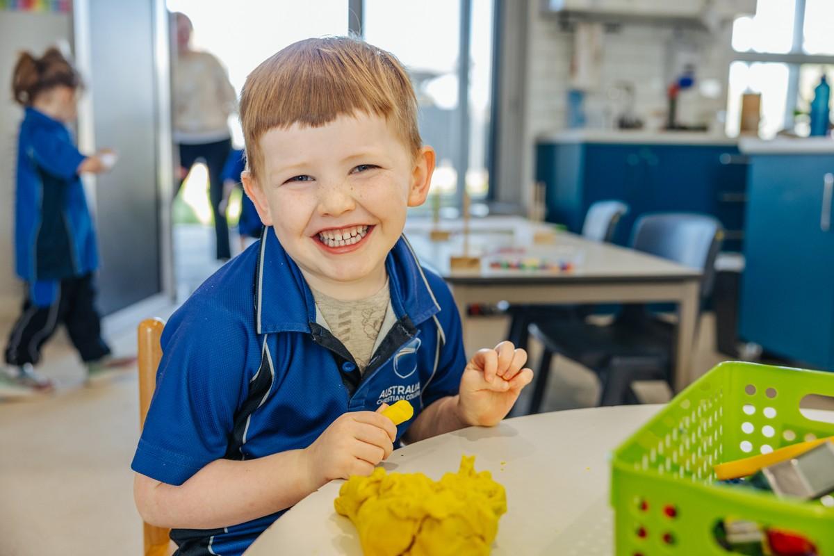 Beaming kindergarten boy enjoying creative play with yellow playdough in a Southlands classroom