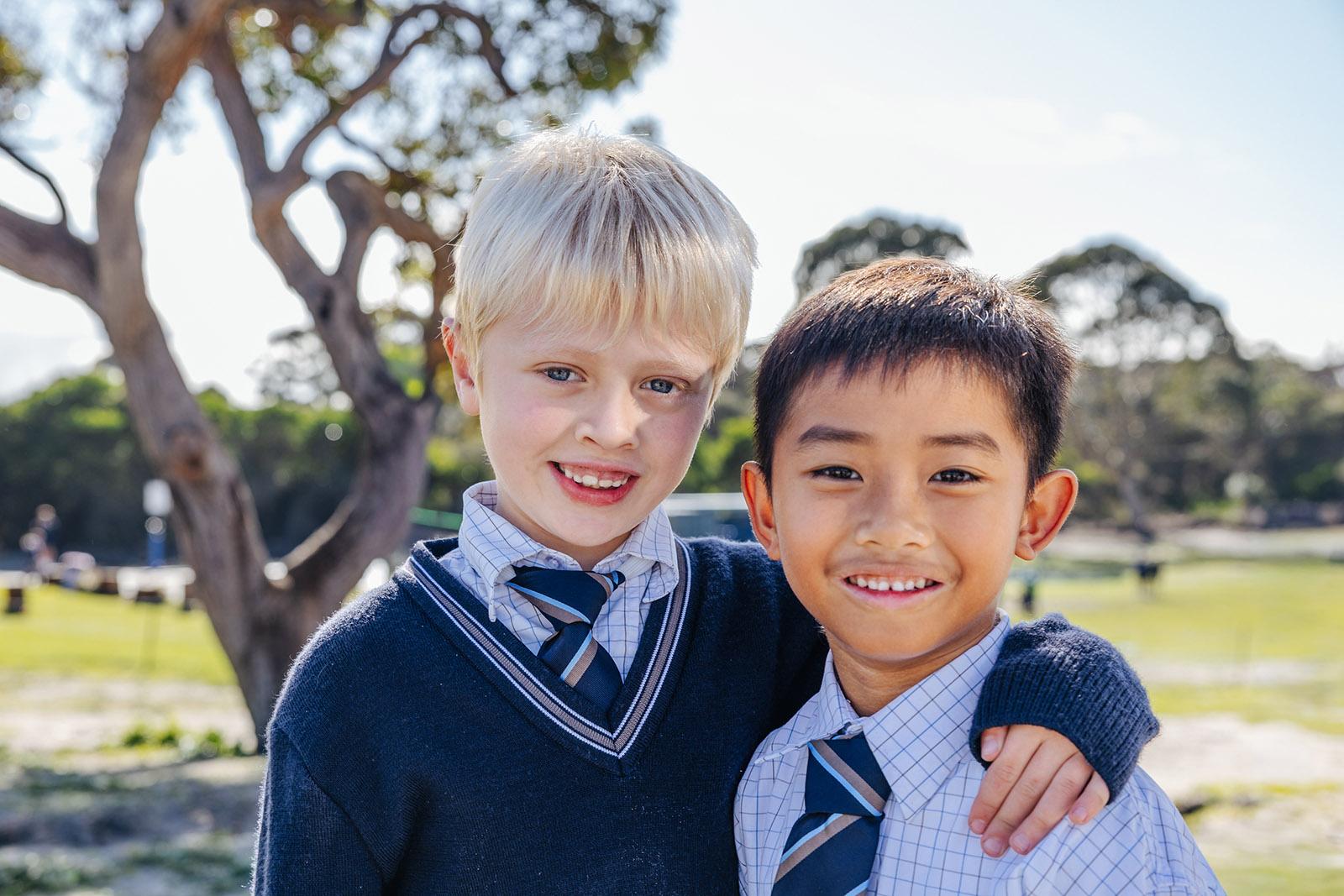 Two primary boys in ACC formal uniforms with arms around each other smiling outdoors at the Albany school