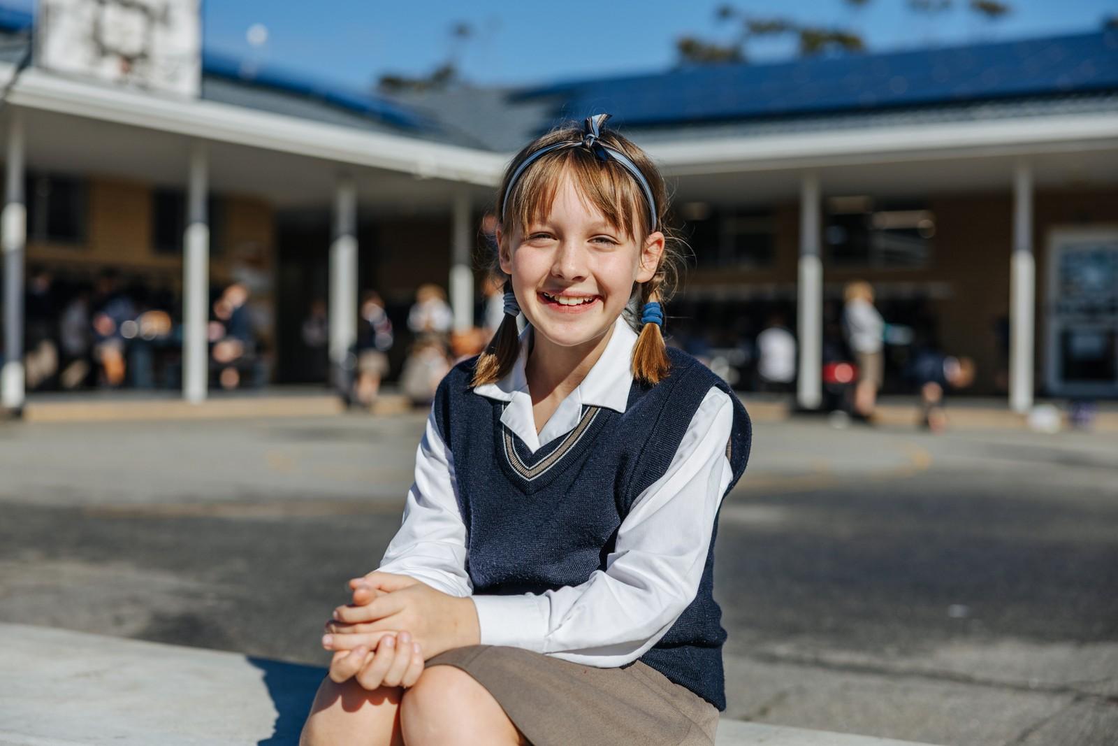 Smiling primary girl in ACC uniform sitting in the school courtyard in Albany
