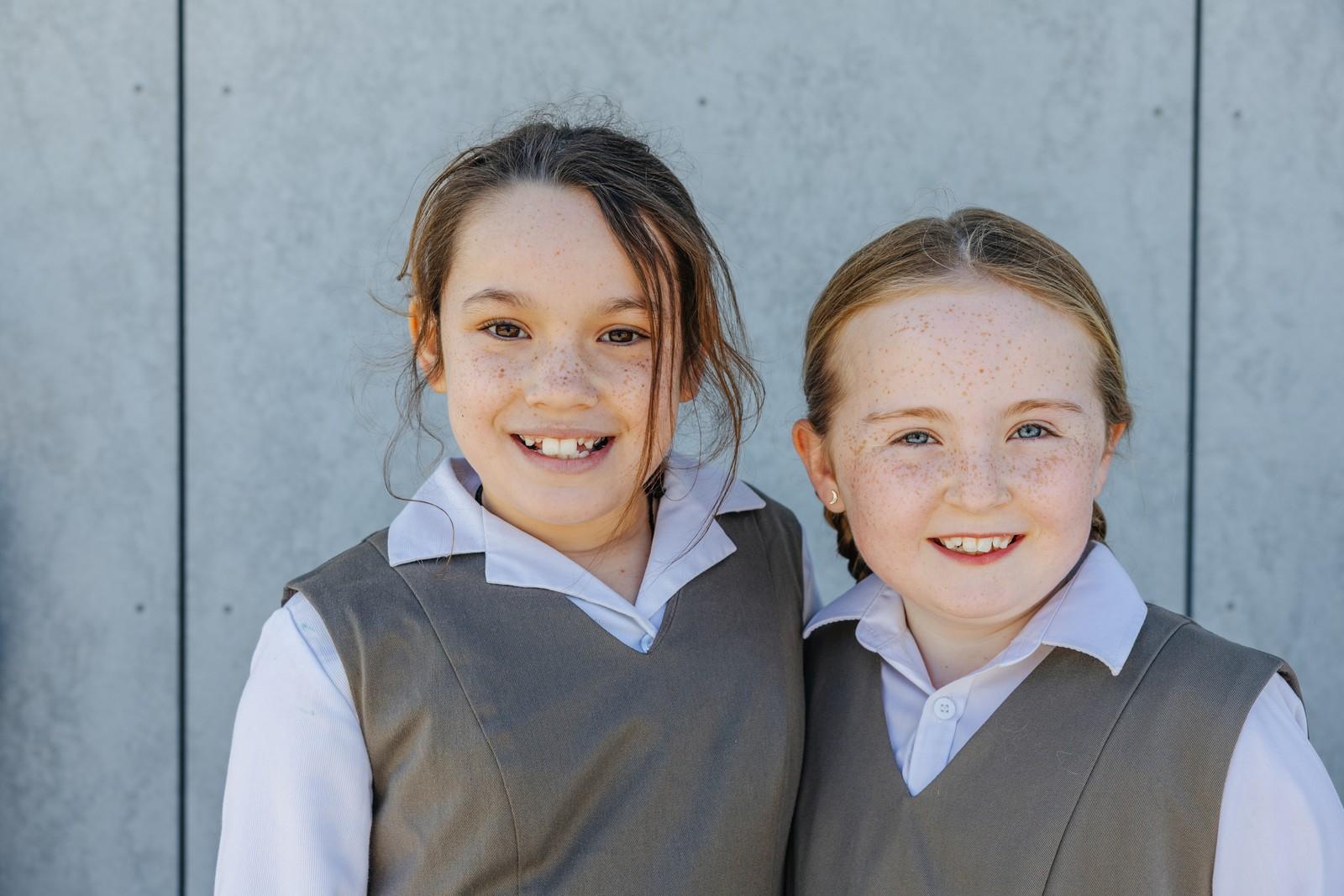 Two primary girls in ACC Southlands uniform smiling together on campus