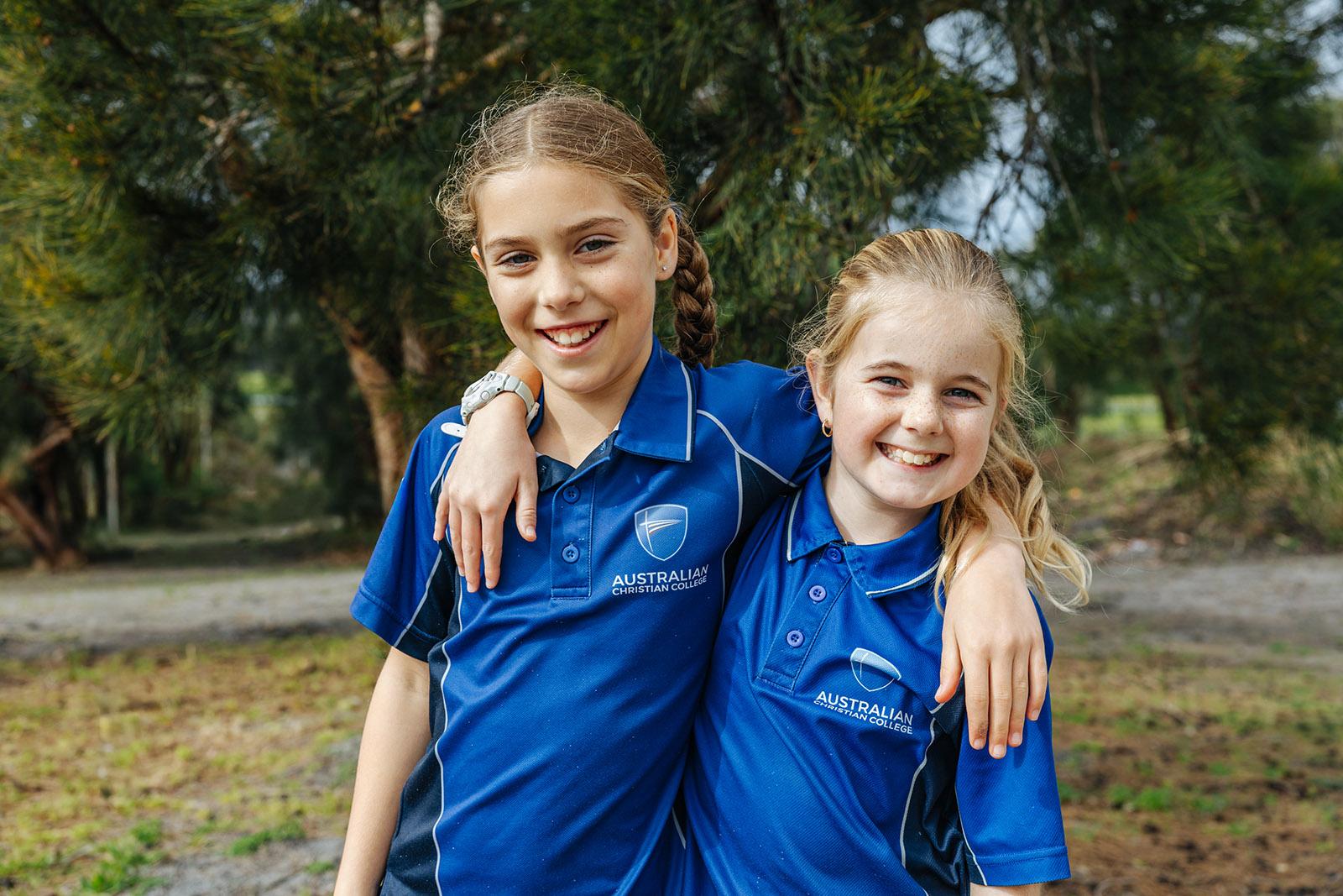 Two smiling primary friends arm-in-arm in ACC Southlands uniforms outdoors at the Albany school