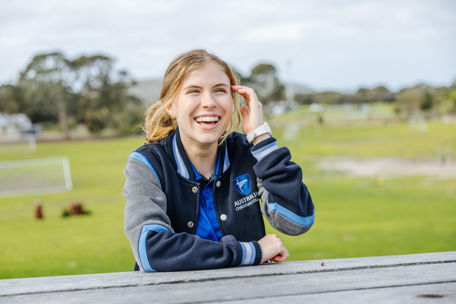 Secondary girl in ACC jacket laughing at a picnic table on school grounds in Albany