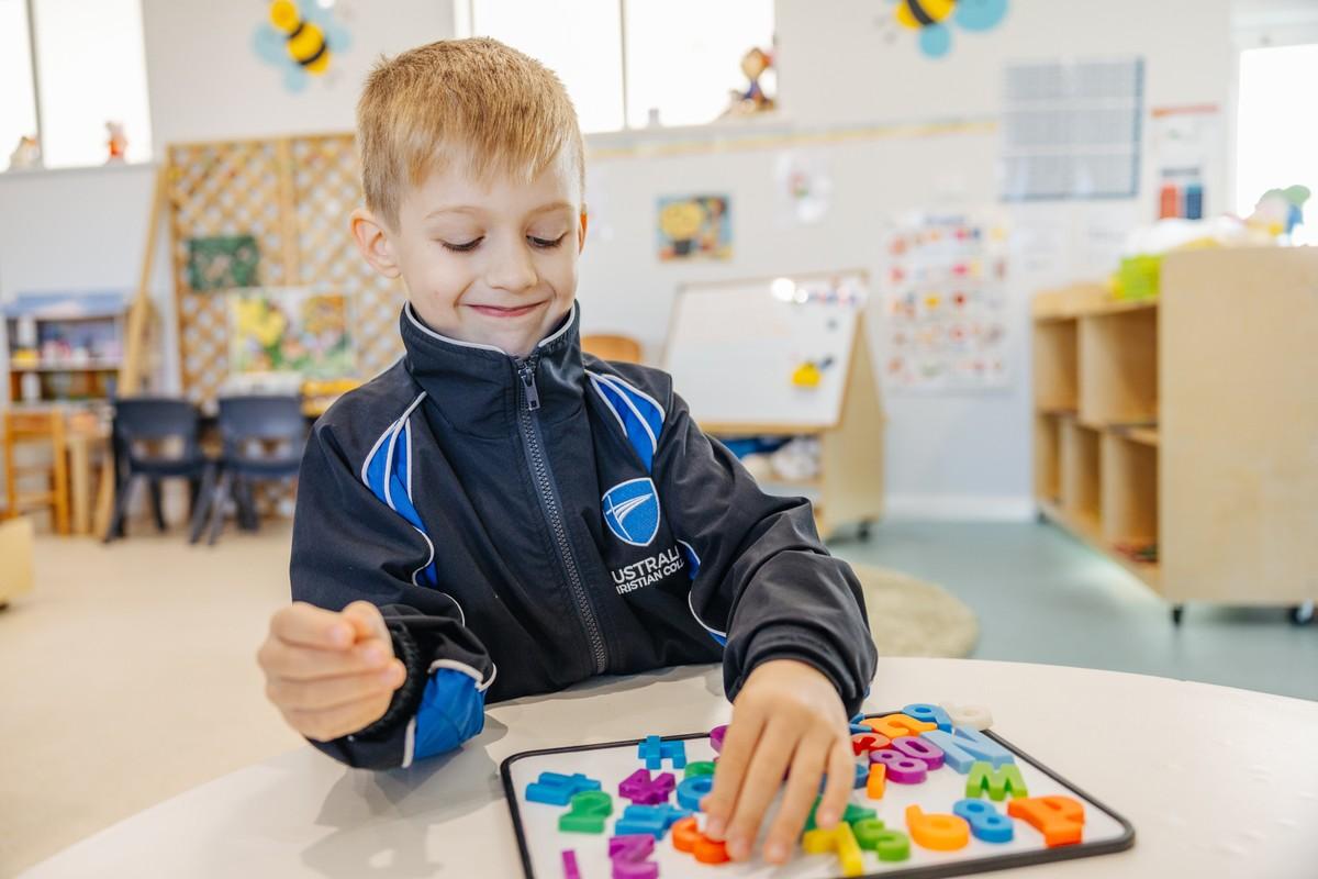 Kindergarten boy sorting colourful magnetic letters and numbers to build literacy skills in a Collingwood Heights classroom