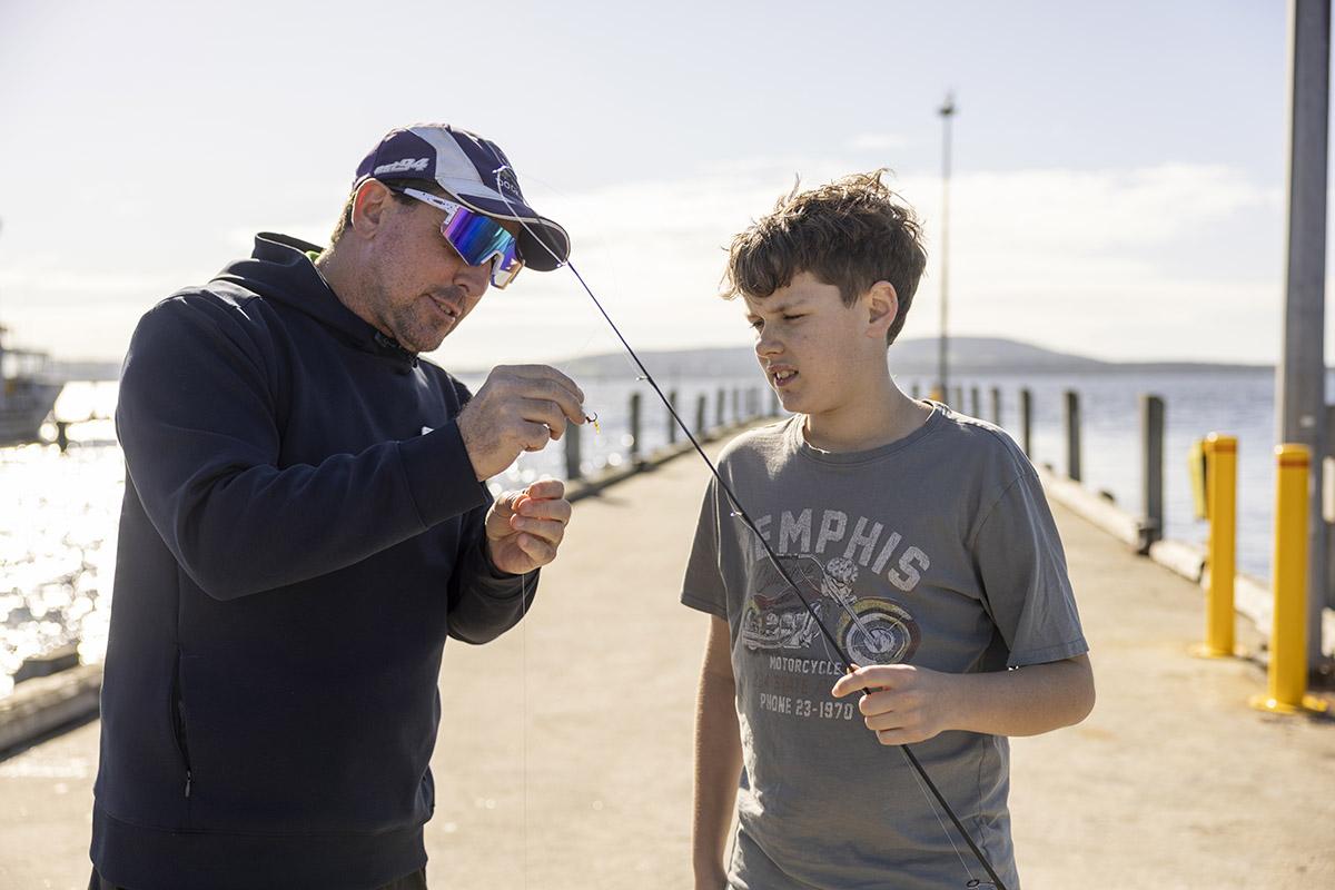 Boarding staff member helping a student thread bait onto a fishing hook by the lake
