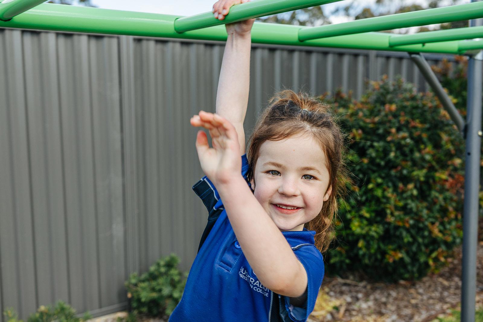 Kindergarten girl swinging from green monkey bars at the Southlands school playground