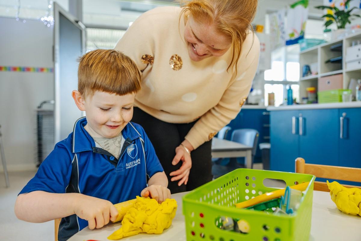 ACC Southlands kindergarten teacher guiding a young boy rolling yellow playdough during a maths activity