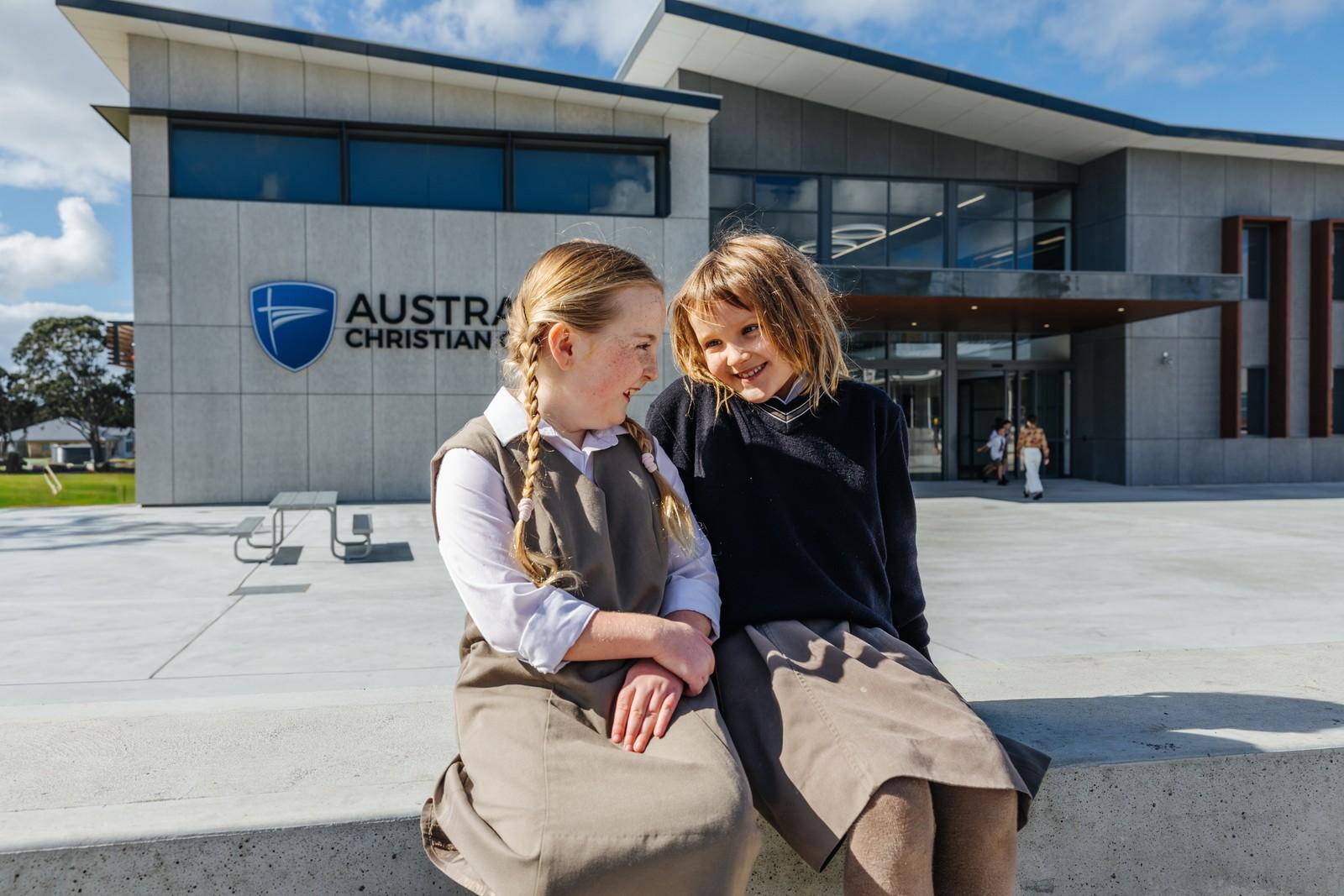 Two primary girls sitting together outside the Australian Christian College Southlands building