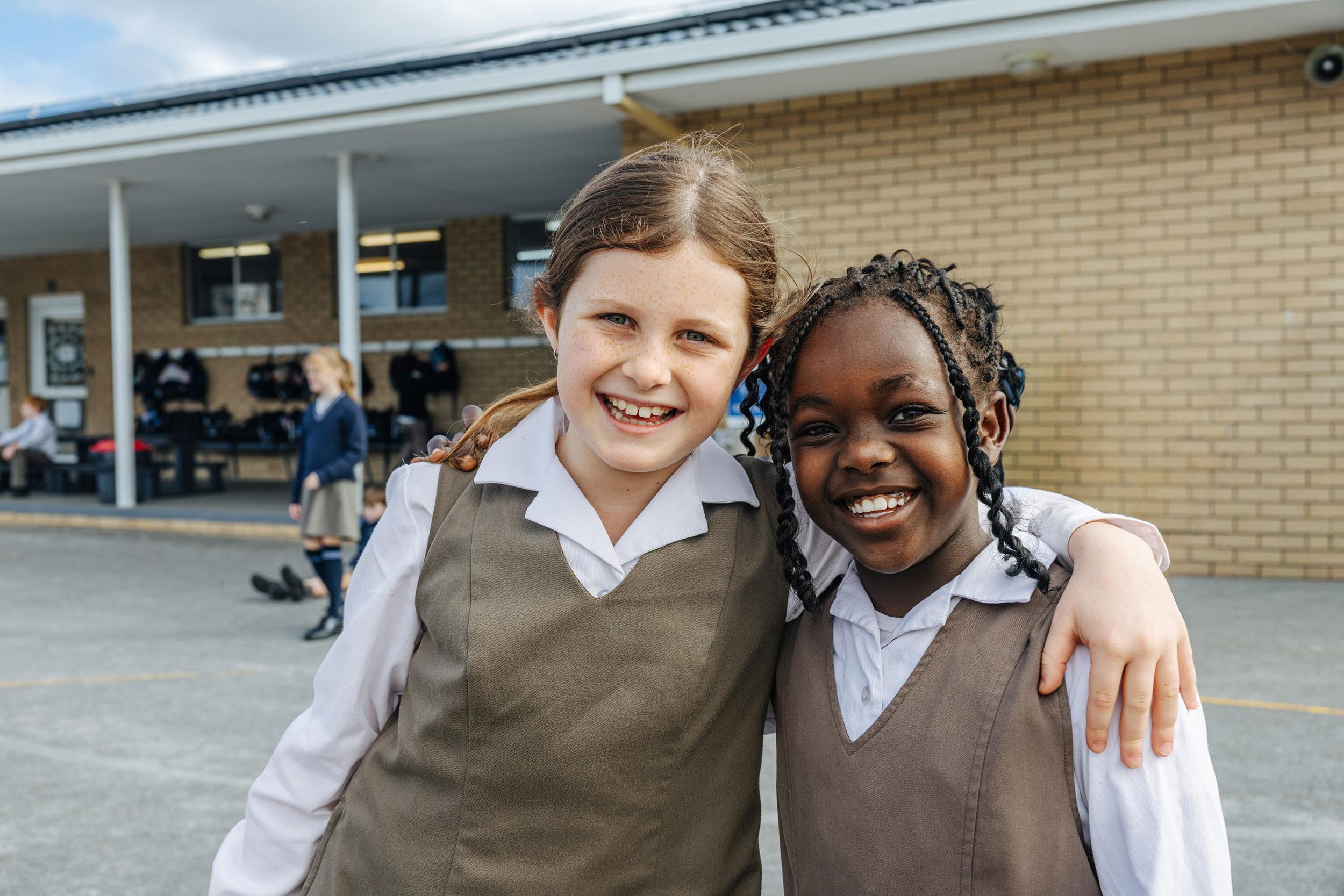 Two smiling primary girls in ACC Southlands formal uniforms arm-in-arm in the school courtyard