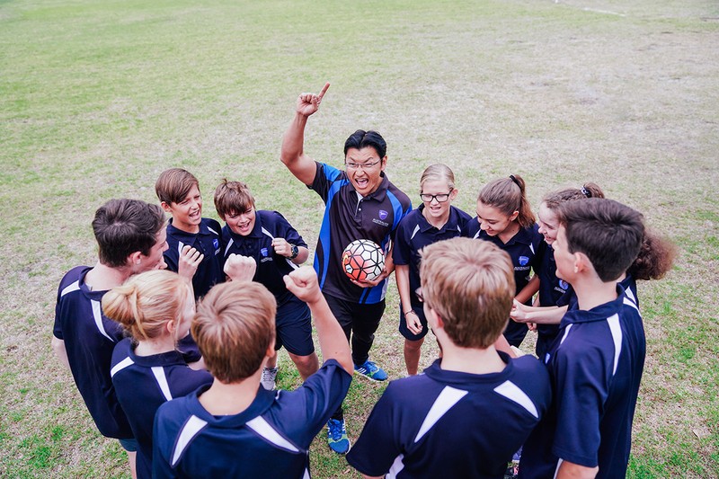 High school sports class in circle around teacher holding soccer ball