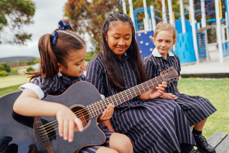Three ACC Southlands girls playing guitar outside