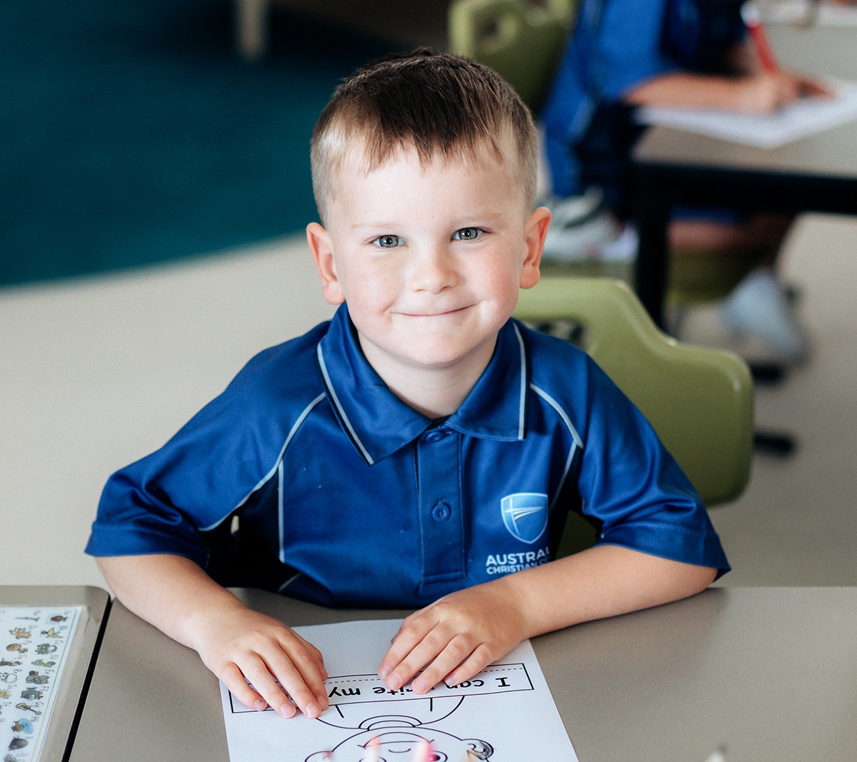 kindergarten boy smiling at camera while colouring in