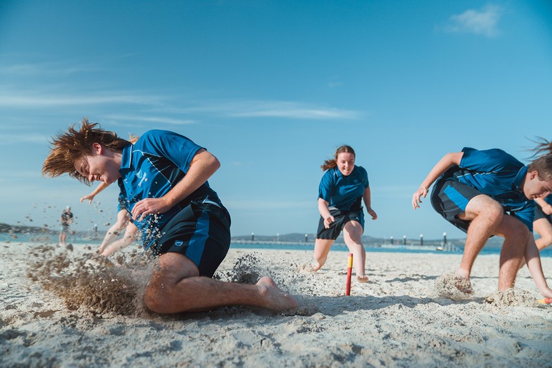 ACC Southlands students in sports uniform on beach playing games