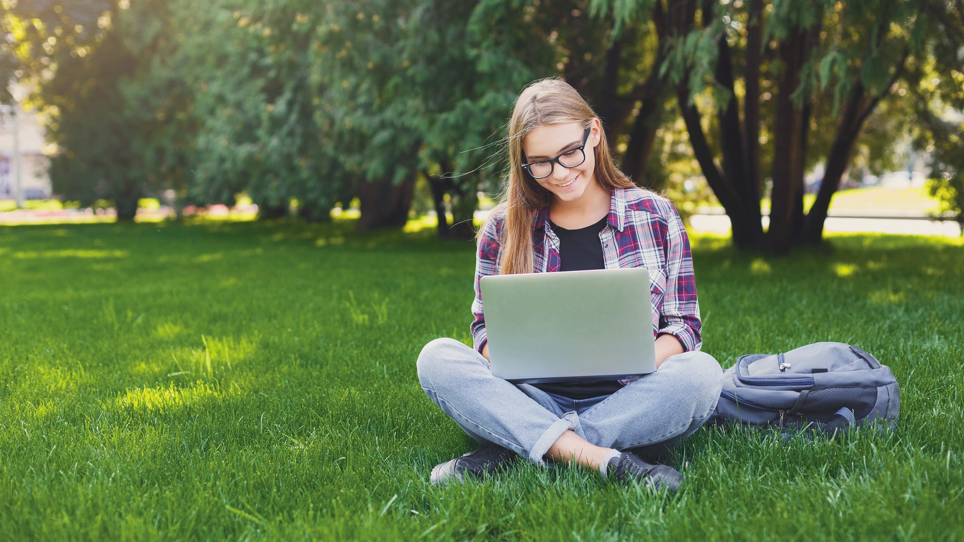 Happy distance education high school student doing online schoolwork while outside on her computer