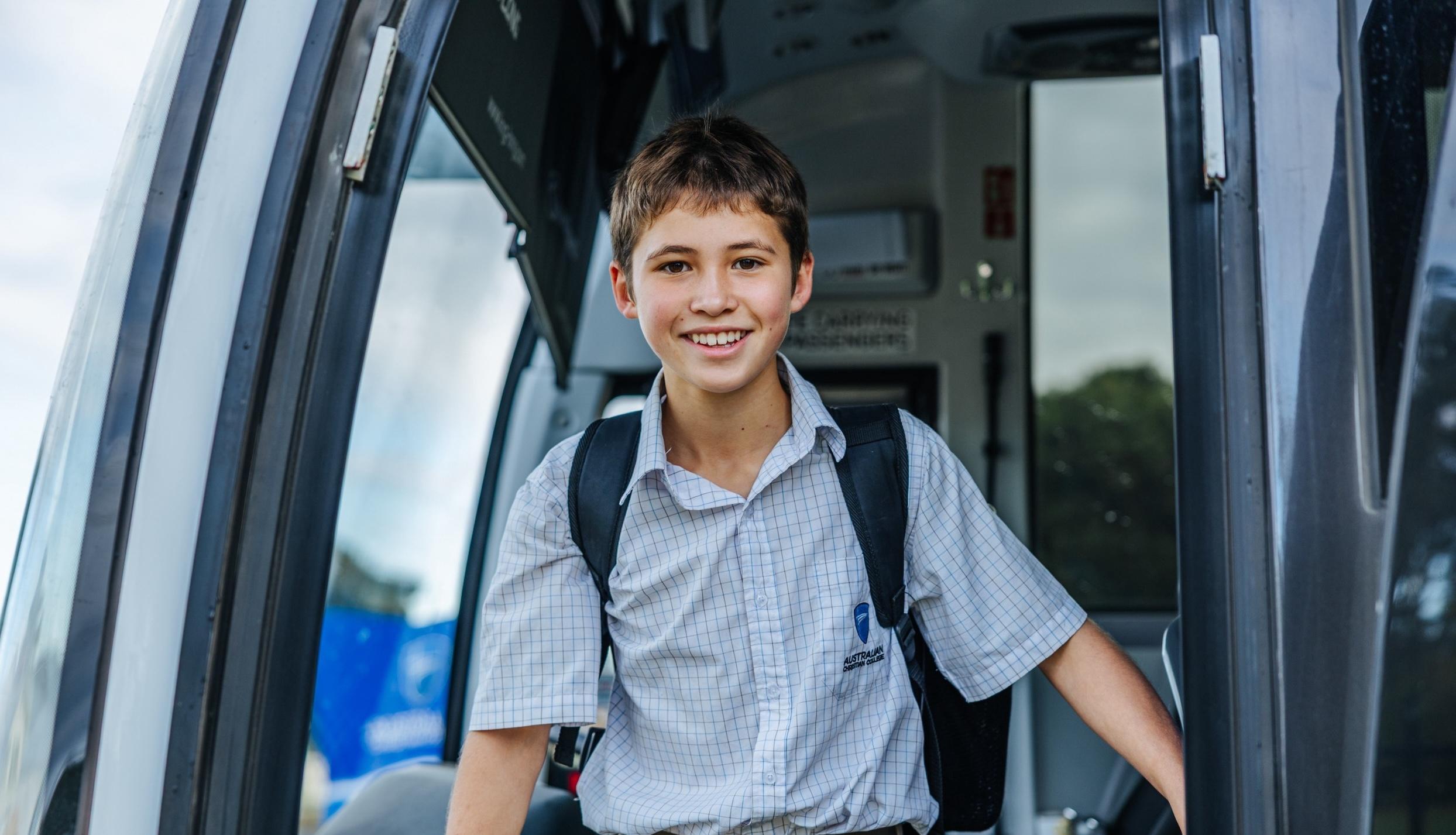 A student in school uniform smiles while stepping off a bus at ACC Swan Hill, ready for