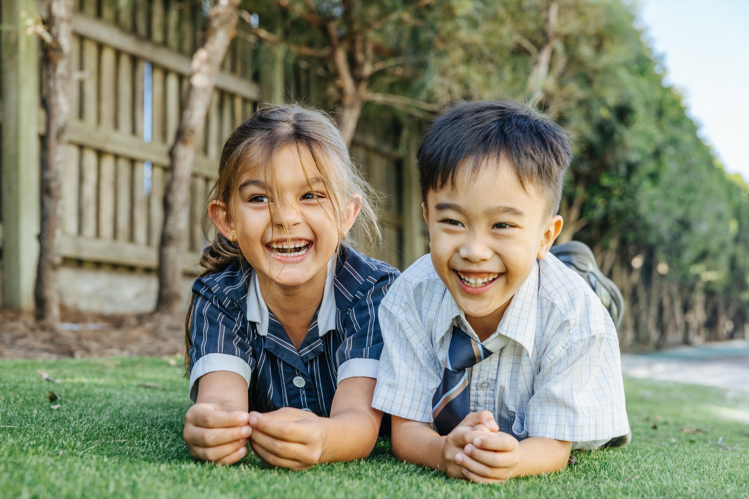 Two primary school students at ACC Swan Hill lie on the grass, smiling and enjoying their time together.