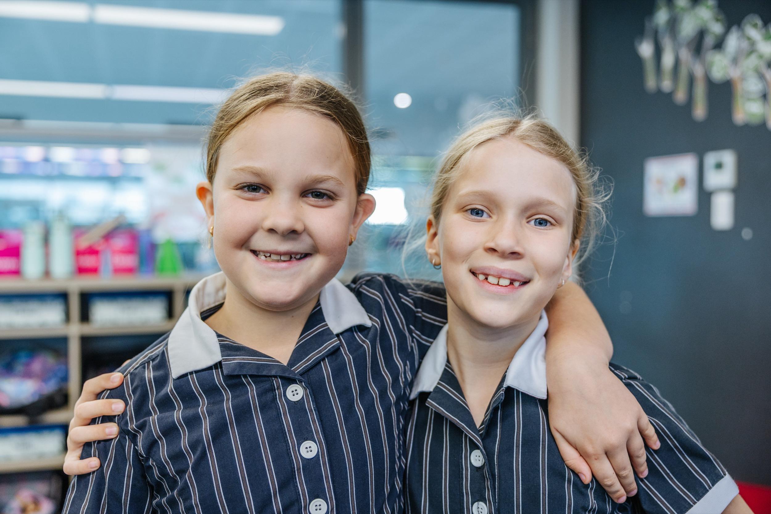 Two students in school uniforms smiling and standing close together with their arms around each other