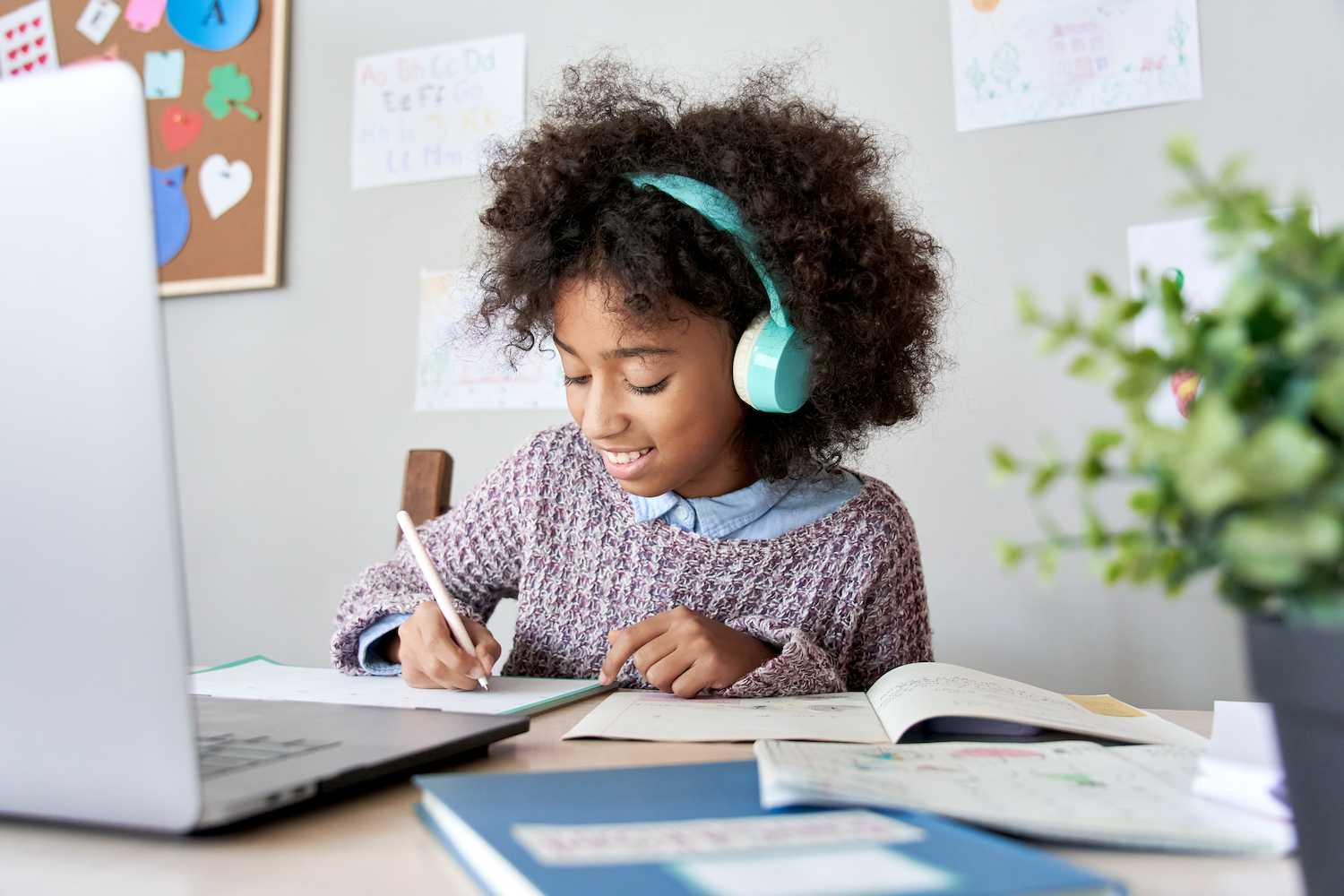 Girl with curly hair wearing jumper and headphones completing distance education online